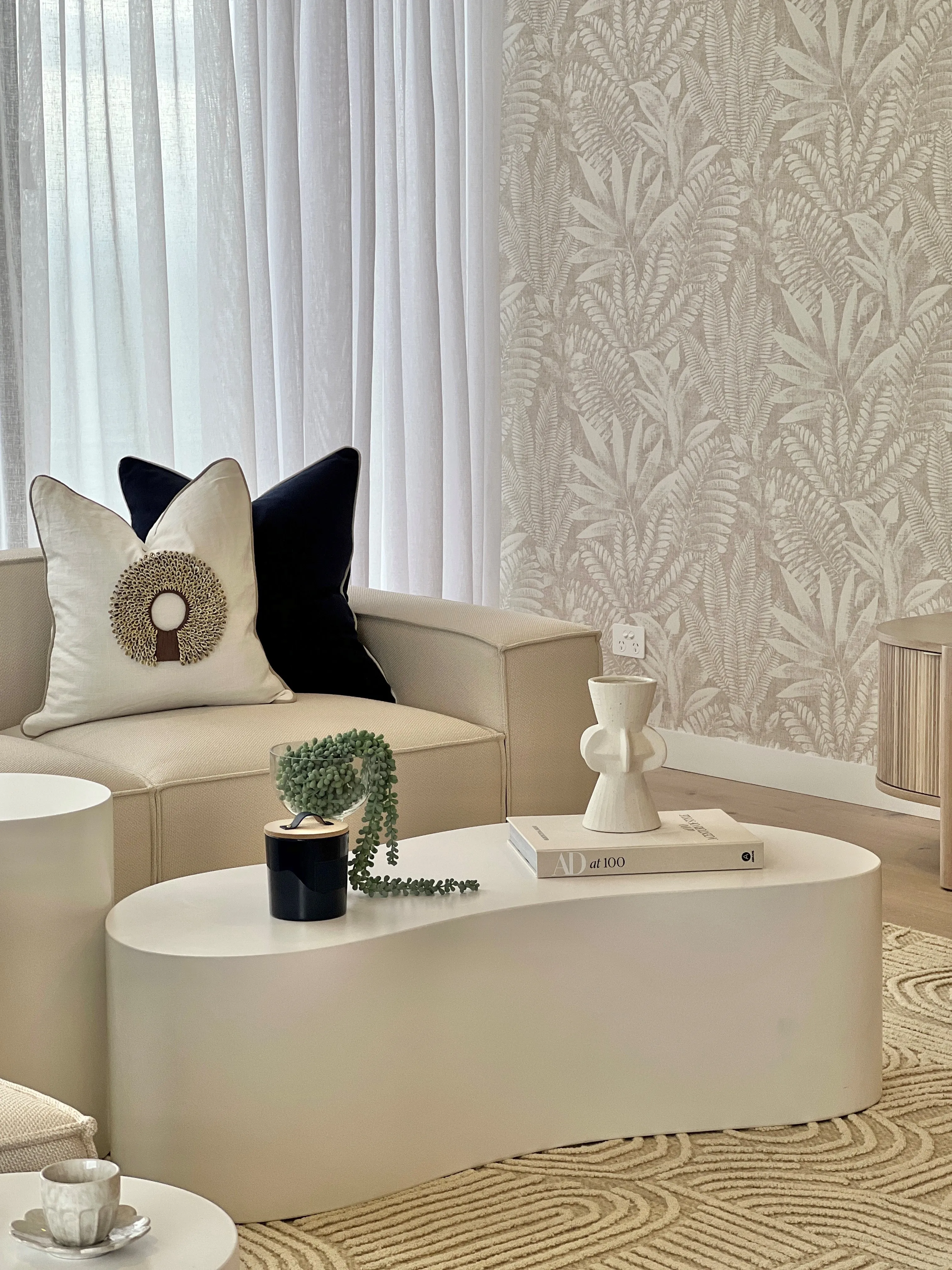 Open-plan living area with cream modular sofa, white organic coffee tables and botanical feature wall